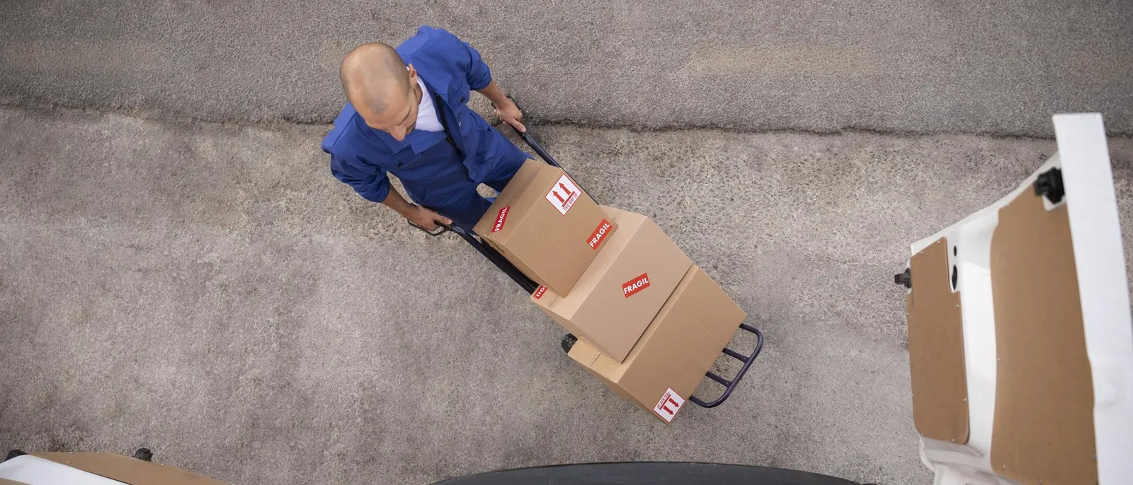 A mover in overalls wheeling packed boxes marked fragile towards an open van