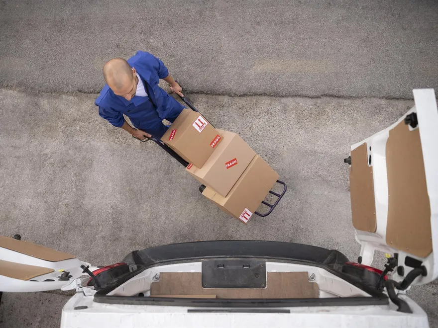 A mover in overalls wheeling sealed boxes on a trolley towards an open van
