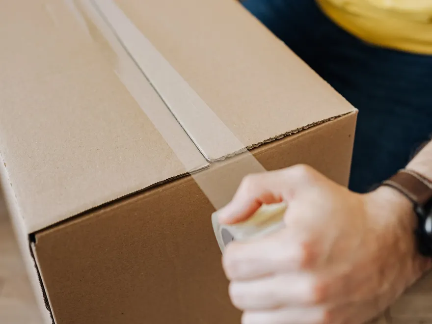 Hands sealing a packed moving box with tape